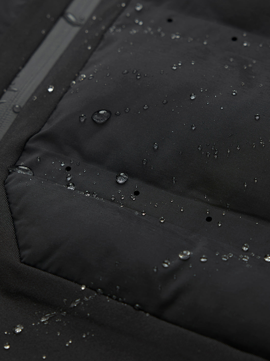 Close up of black LVS fabric with water droplets, zipper, and white wing logo on the collar.