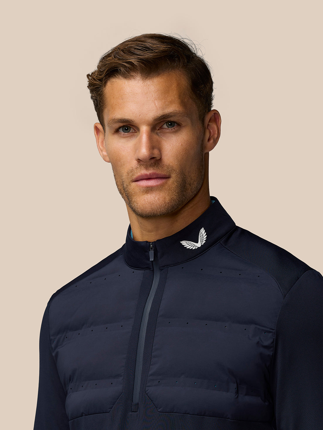 Male model wearing midnight navy golf half zip top with wing logo at the collar