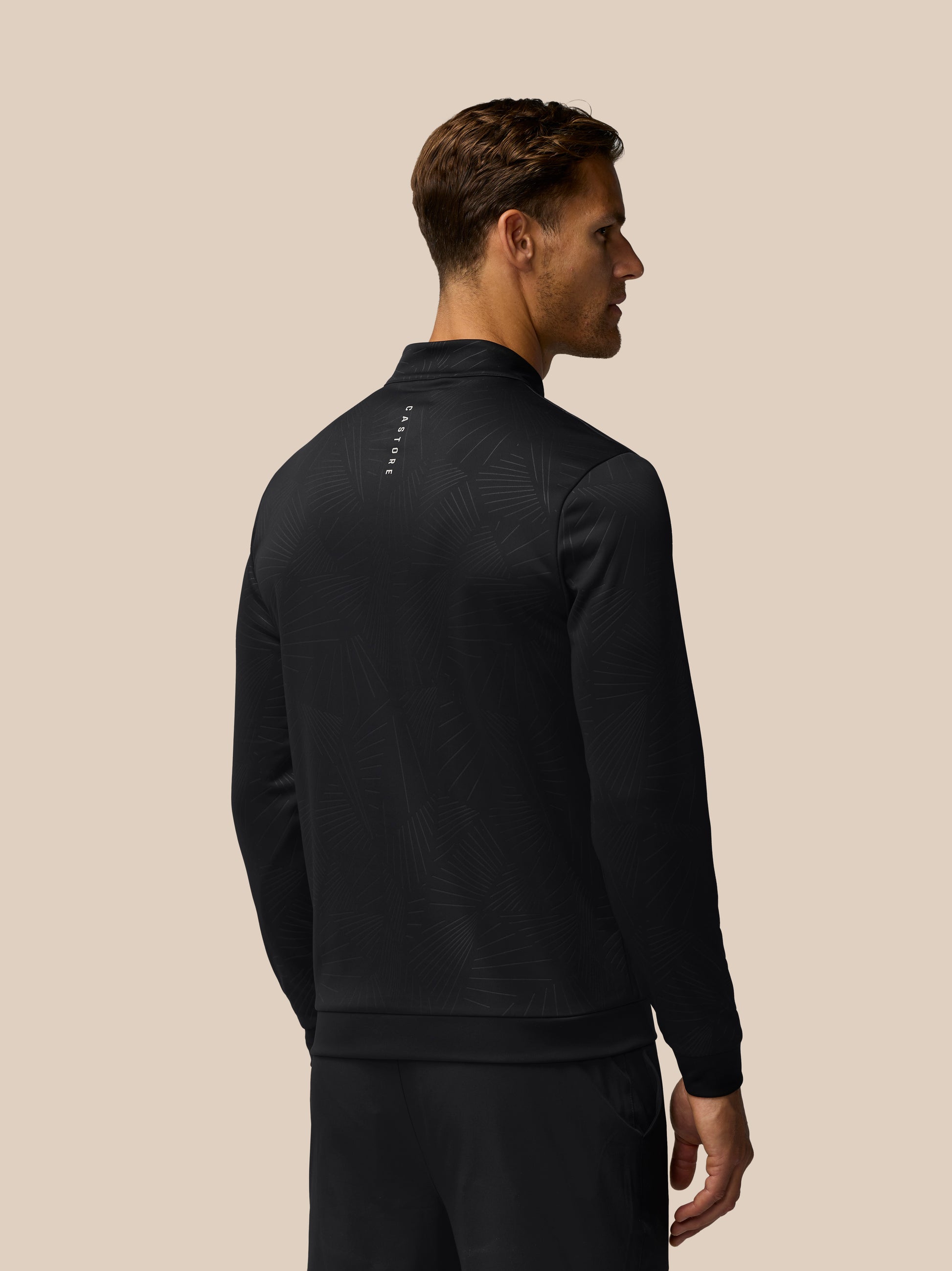 Man wearing black golf quarter-zip top with a subtle line pattern; back view shows Castore branding along the spine.
