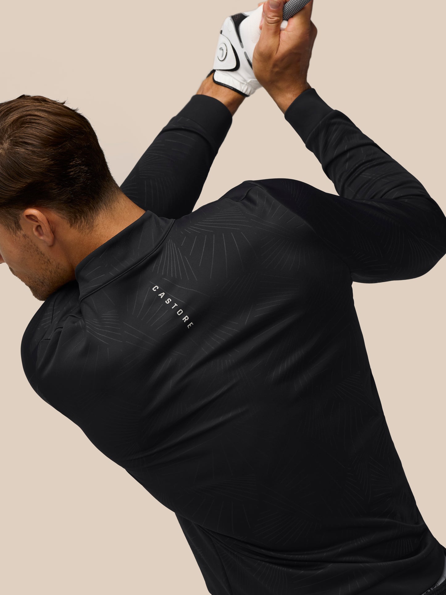 Golfer wearing Castore Golf Club Classic quarter-zip top in black with a subtle linear pattern while swinging
