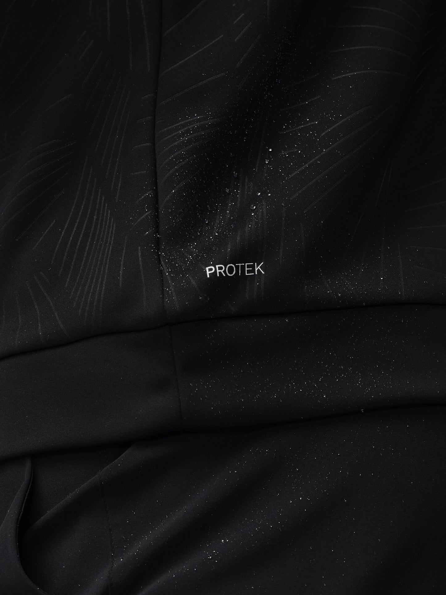 Close-up of black fabric with a subtle diagonal print, water droplets, and PROTEK branding on a golf top.