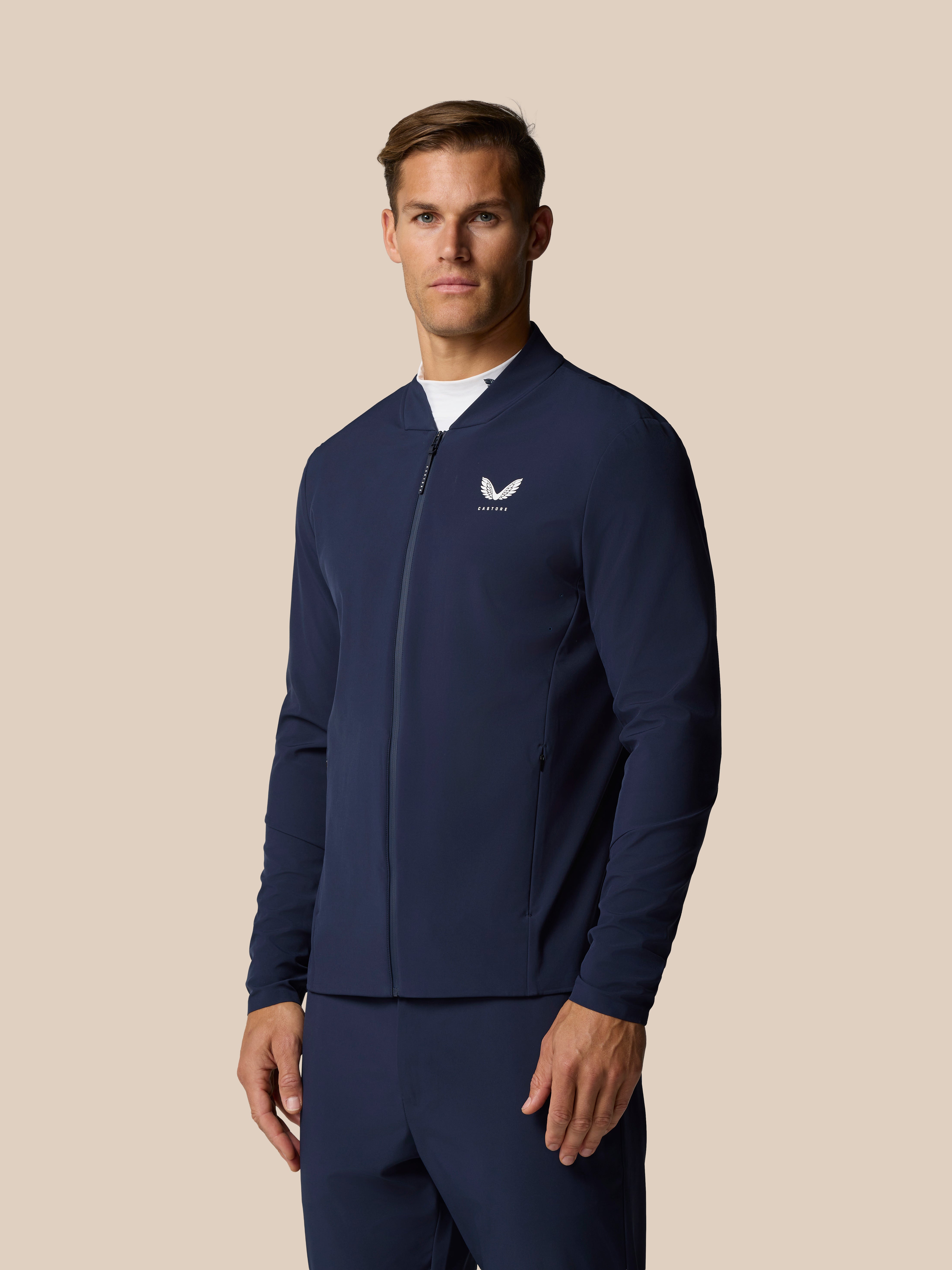Male model wearing midnight navy Golf Pinnacle LVS Jacket with full front zip and Castore logo on left chest