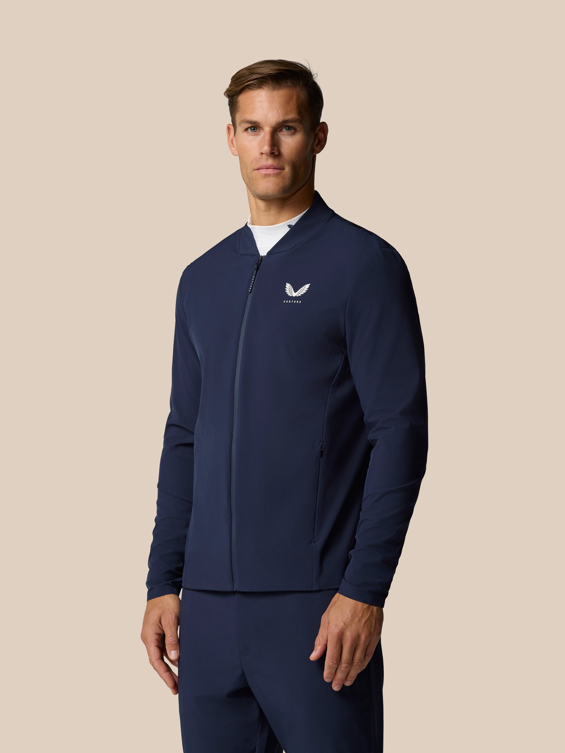 Male model wearing midnight navy Golf Pinnacle LVS Jacket with full front zip and Castore logo on left chest