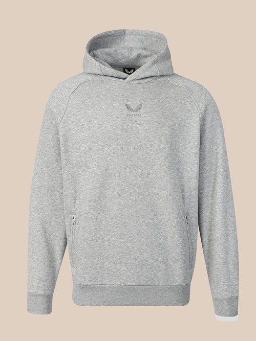 A light gray heather pullover hoodie with a small dark gray winged logo on the center chest, displayed against a solid beige background.