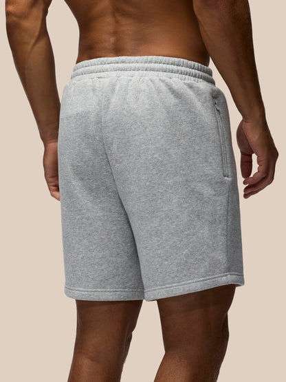 A close-up back view of a person wearing light heather gray sweat shorts against a solid beige background.