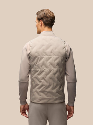 A man shown from the back wearing a light taupe quilted vest over a matching long-sleeve shirt and trousers, set against a solid beige background.