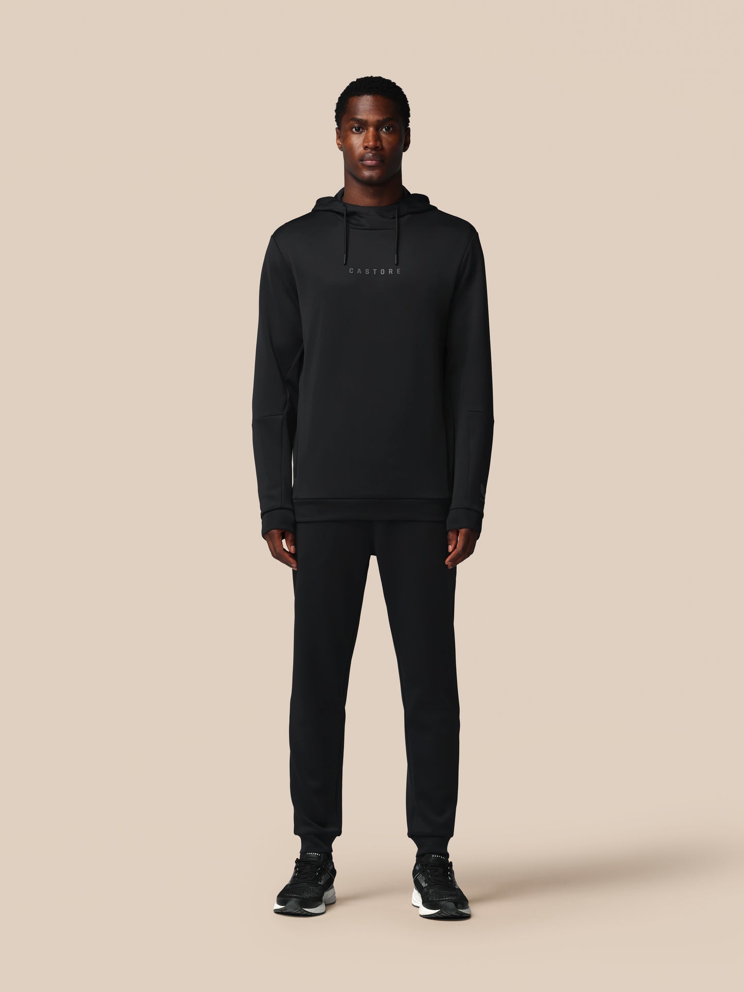 Person wearing a black hoodie and pants on a beige background