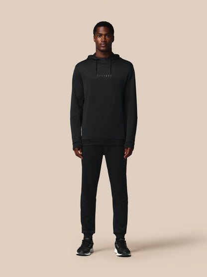 Person wearing a black hoodie and pants on a beige background