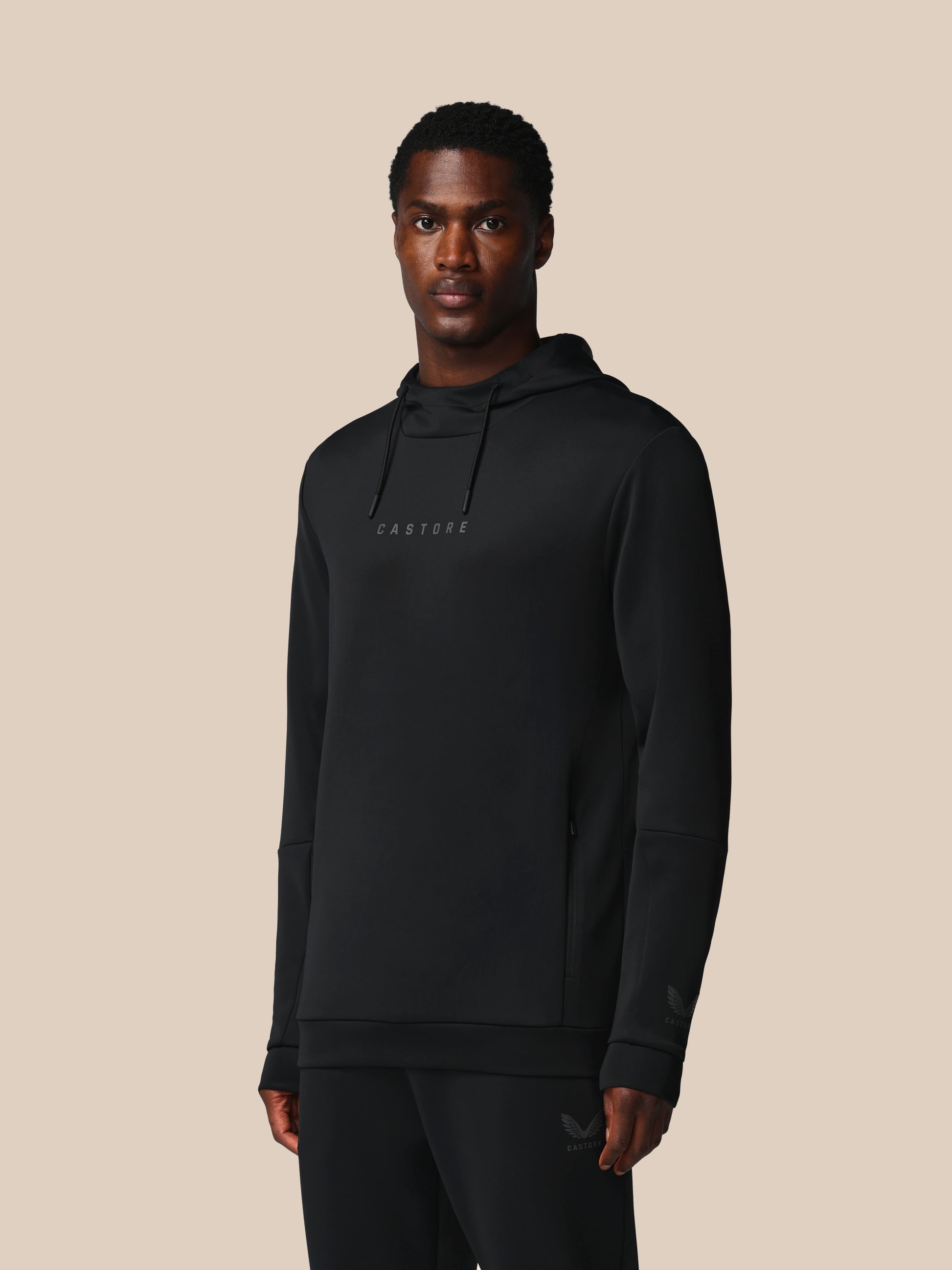 Man wearing a black hoodie with a brand logo on a beige background