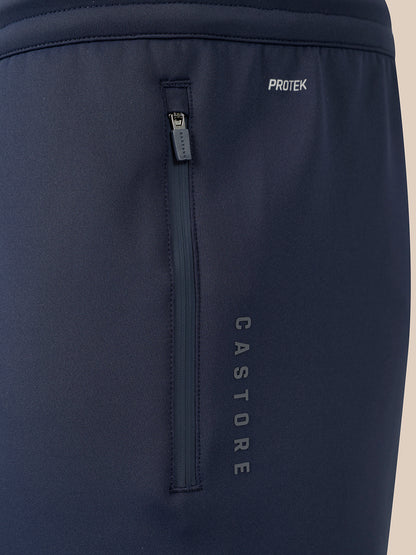 Close-up of dark navy athletic pants showing a vertical zippered pocket with the vertical brand name CASTORE and a small horizontal zip pocket with the brand name PROTEK.