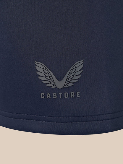 Close-up of a navy blue garment with a tonal gray winged logo and the word CASTORE centered on the chest, against a light beige background.