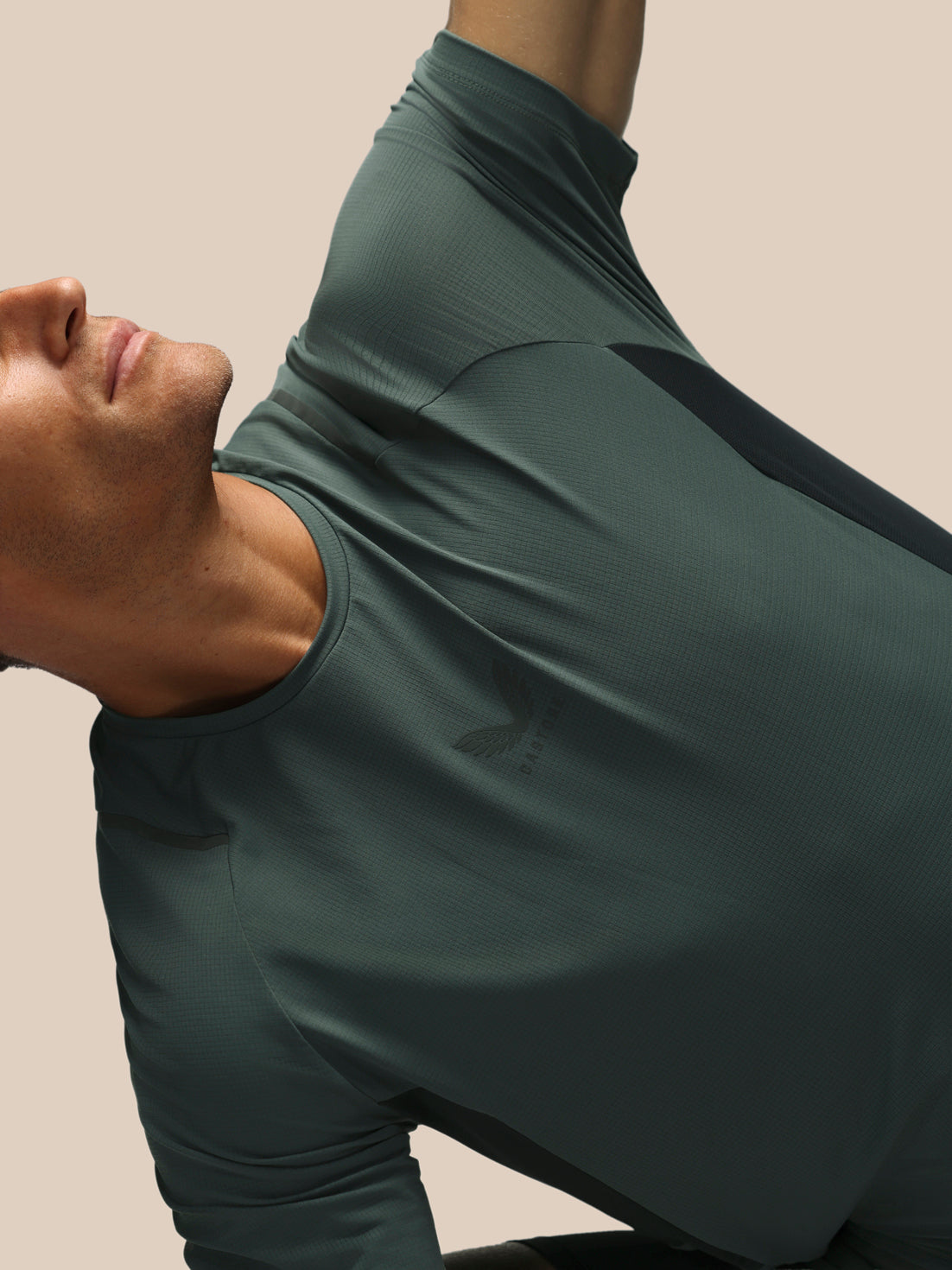 A close-up of a man wearing a dark green athletic short sleeve shirt, shown from the side and back against a solid beige background.