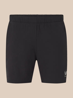 Black athletic shorts with an elastic waistband and a small white embroidered logo on the lower left leg, shown against a solid beige background.