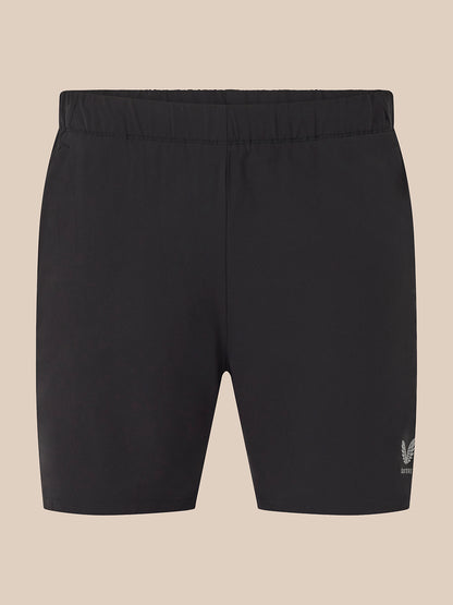 Black athletic shorts with an elastic waistband and a small white embroidered logo on the lower left leg, shown against a solid beige background.