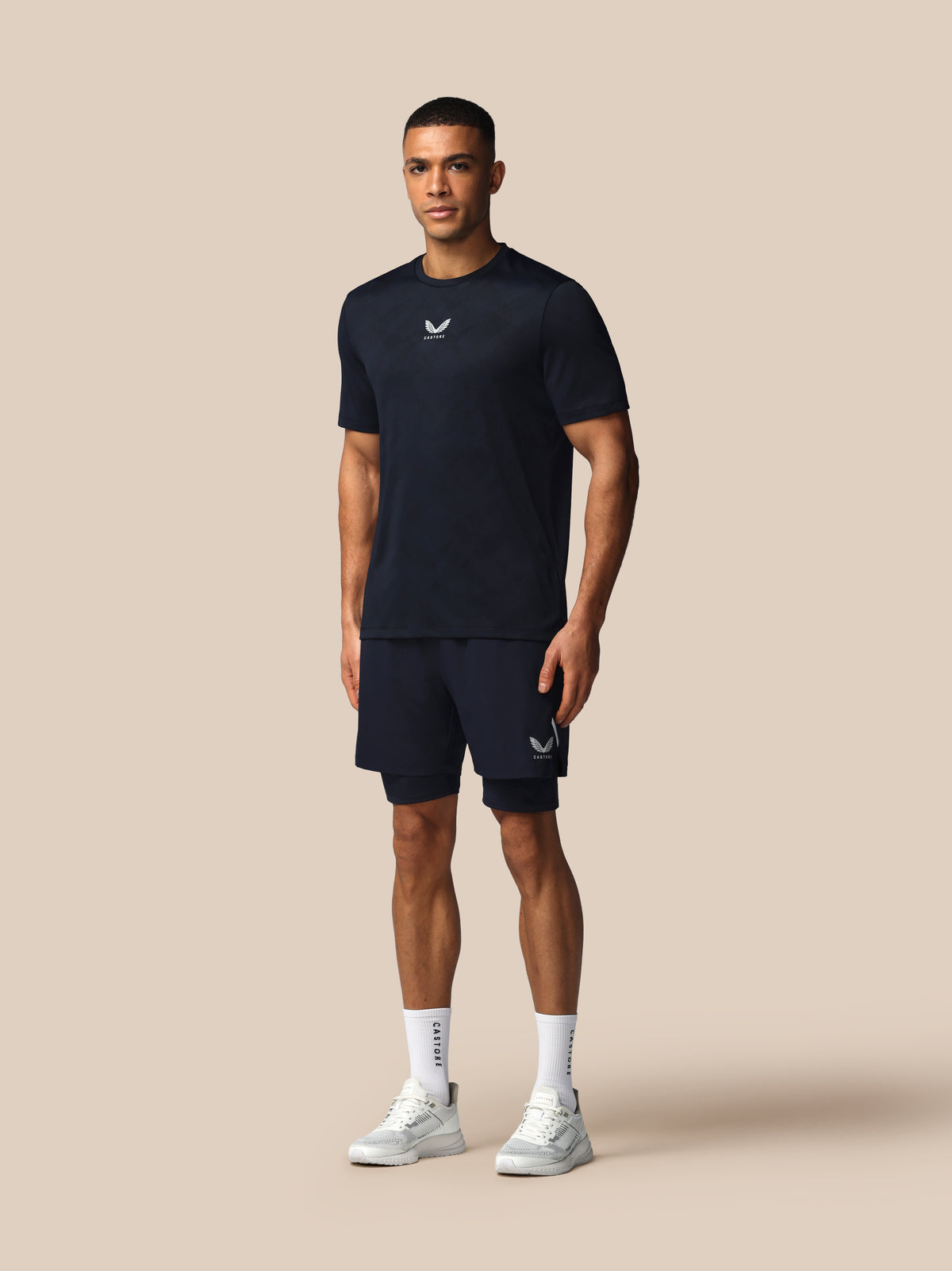 Man wearing a navy athletic outfit with a logo on a beige background