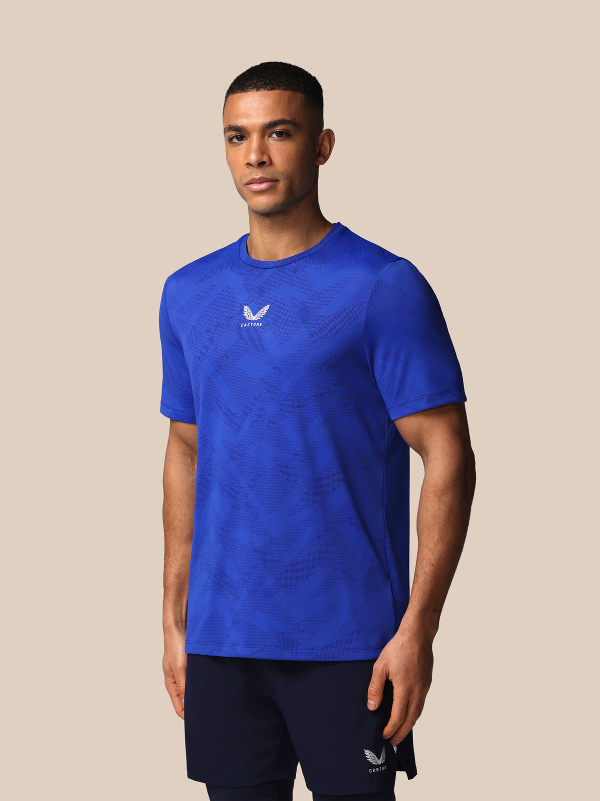 Man wearing a blue athletic shirt with a logo on a beige background