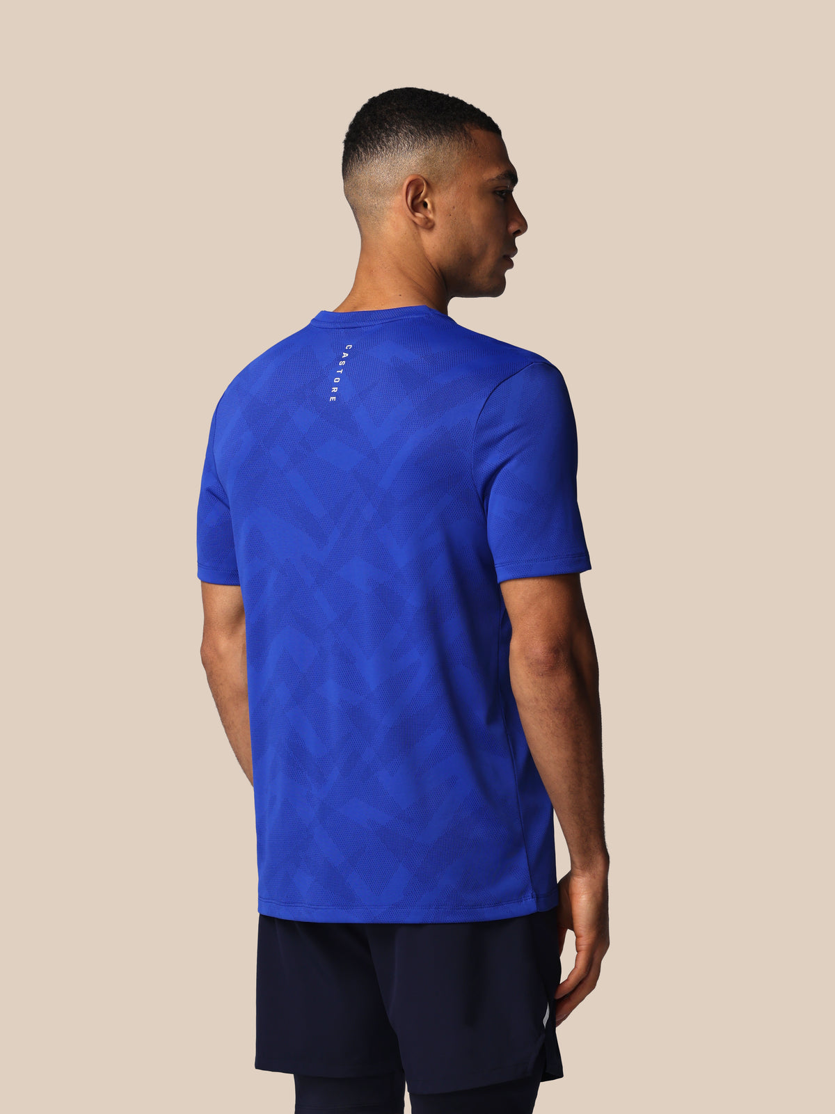 Man wearing a blue athletic shirt and black shorts on a beige background