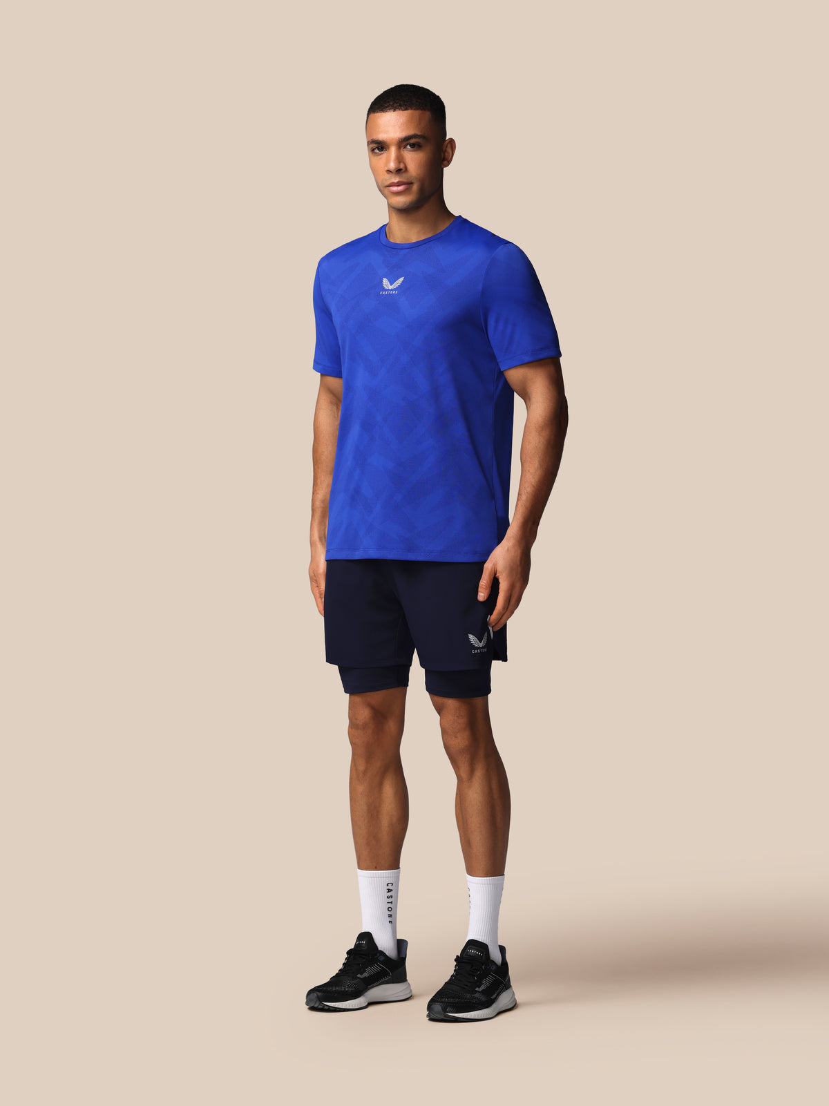 Man wearing a blue athletic shirt and black shorts on a beige background