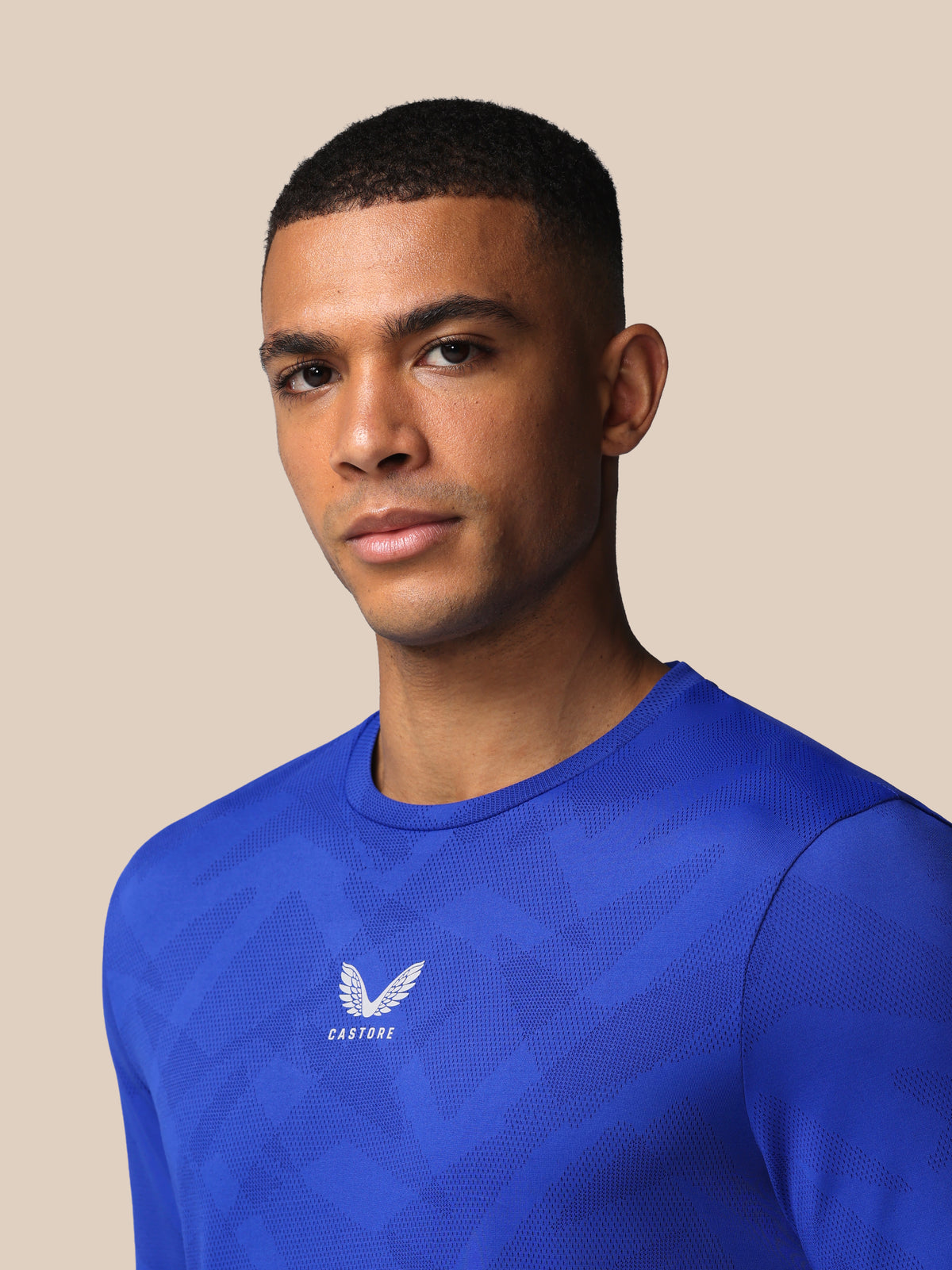 Man wearing a blue athletic shirt with a logo on a beige background