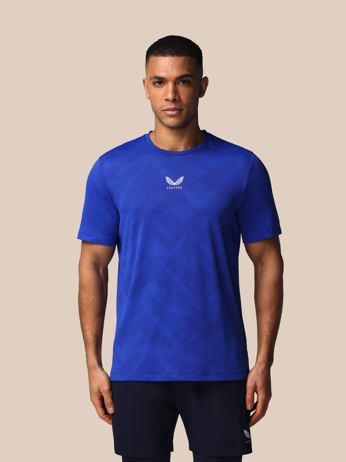 Man wearing a blue athletic shirt with a logo on a beige background
