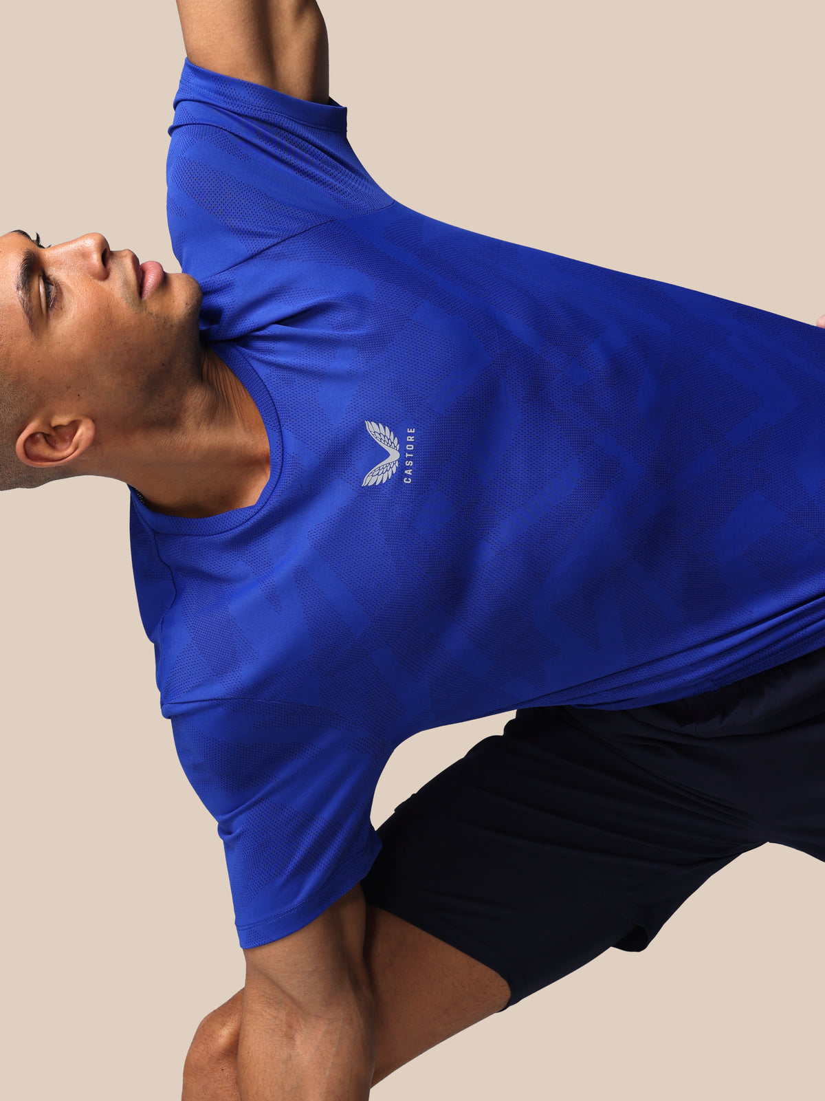 Person wearing a blue athletic shirt with a logo on a beige background