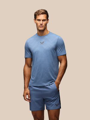 A man modeling a light blue athletic t-shirt and matching shorts with a dark gray Castore logo, set against a solid beige background.