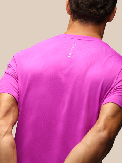 A man viewed from behind wearing a bright pink short-sleeve athletic t-shirt with a small vertical white 'CASTORE' logo on the upper back, set against a solid beige background.