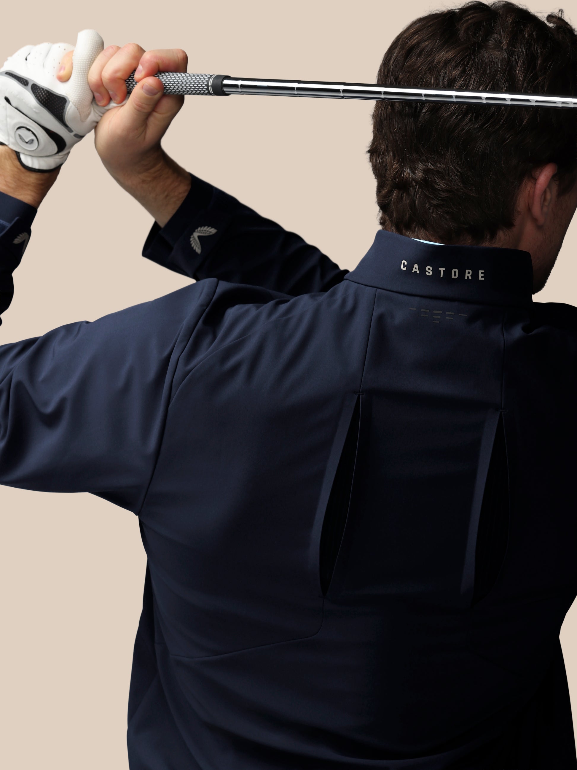 Side view of man wearing navy LVS woven golf jacket holding a golf club overhead against a beige background
