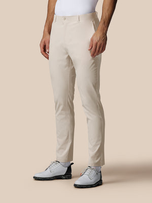 Lower body shot of a model in cream golf trousers with white polo and white sneakers