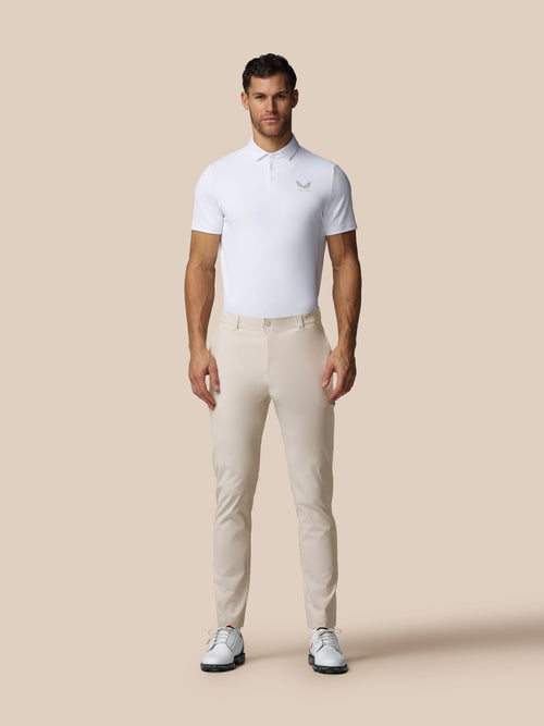 Male model wearing cream golf trousers and white polo against a beige background