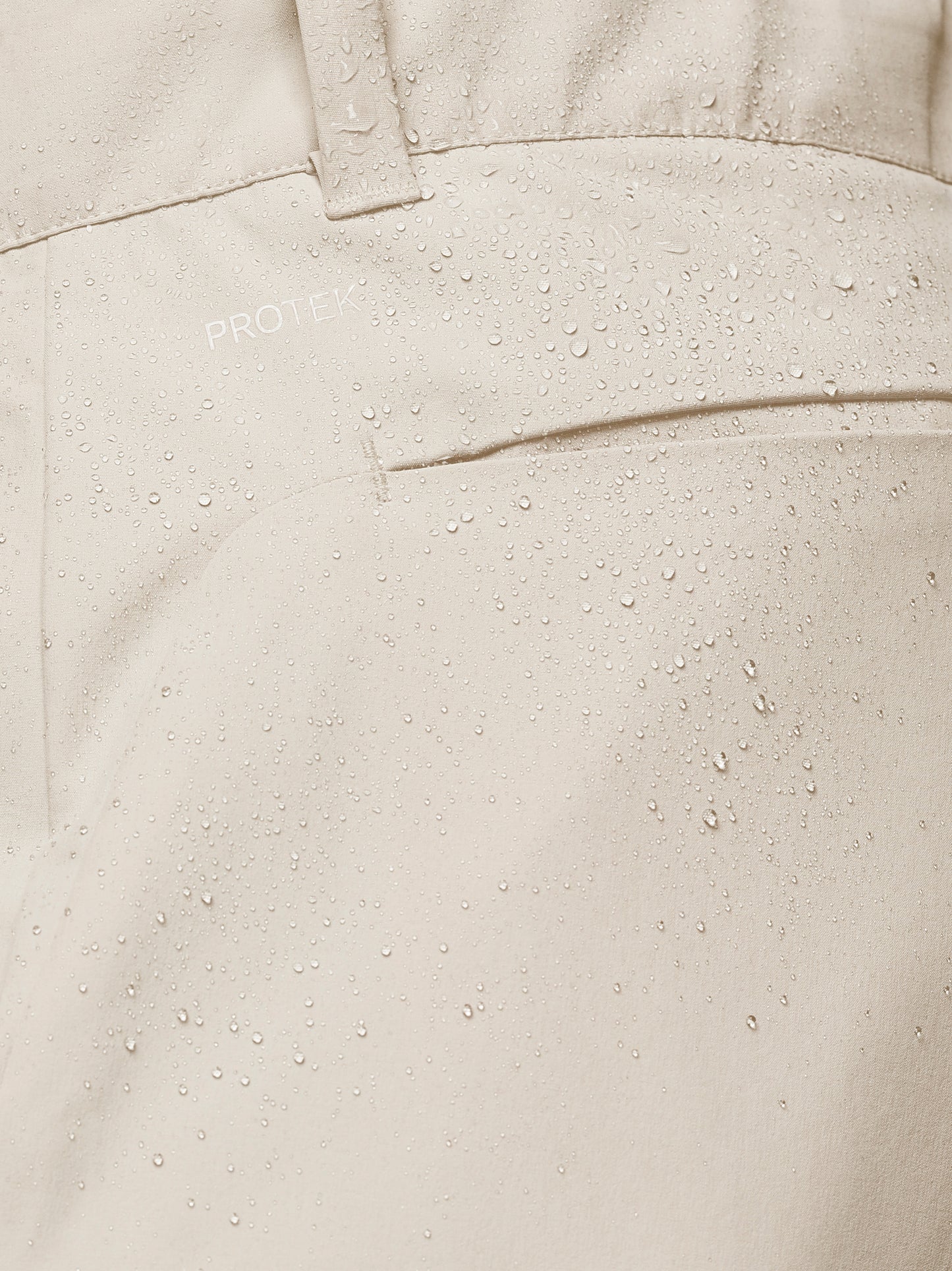 Close-up of cream golf trouser fabric with water droplets and ProTek branding.