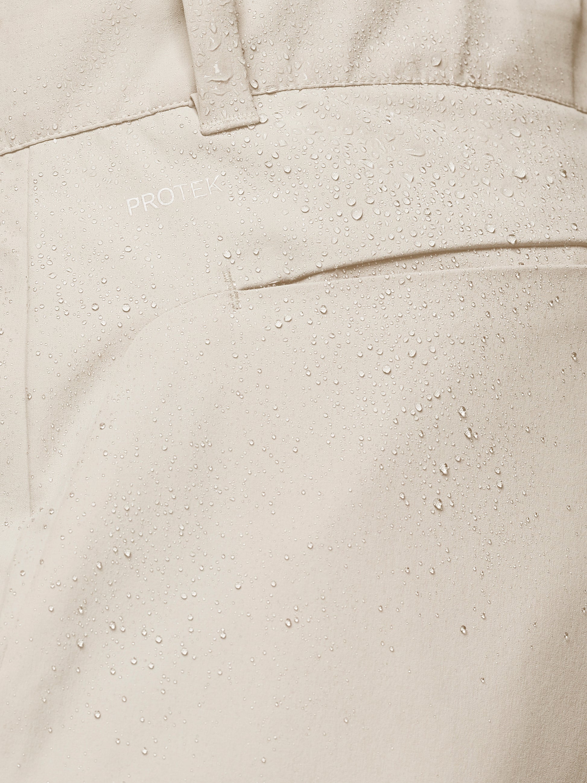 Close-up of cream golf trouser fabric with water droplets and ProTek branding.