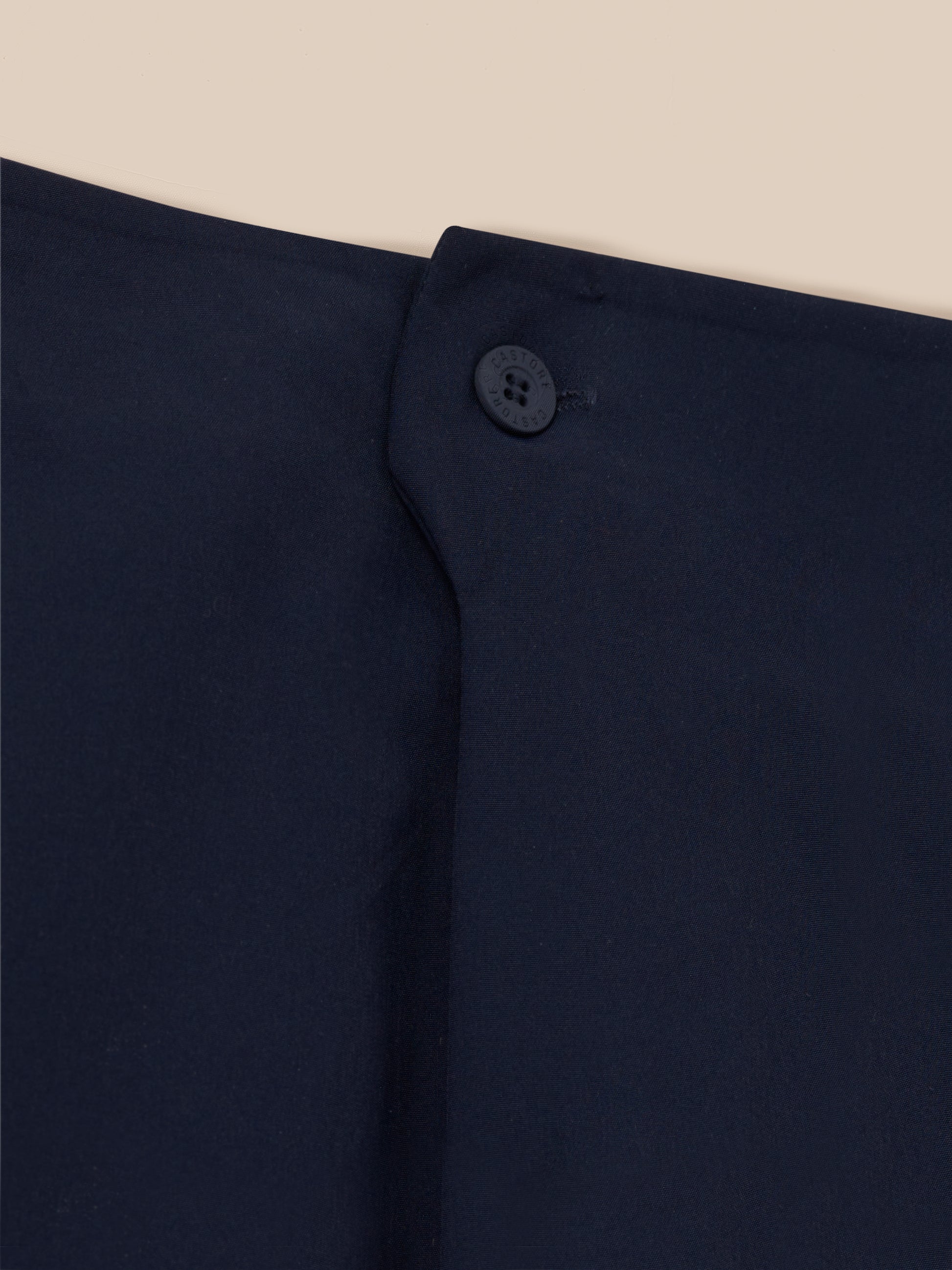 Close up of navy golf trousers waistband button embossed with Castore logo
