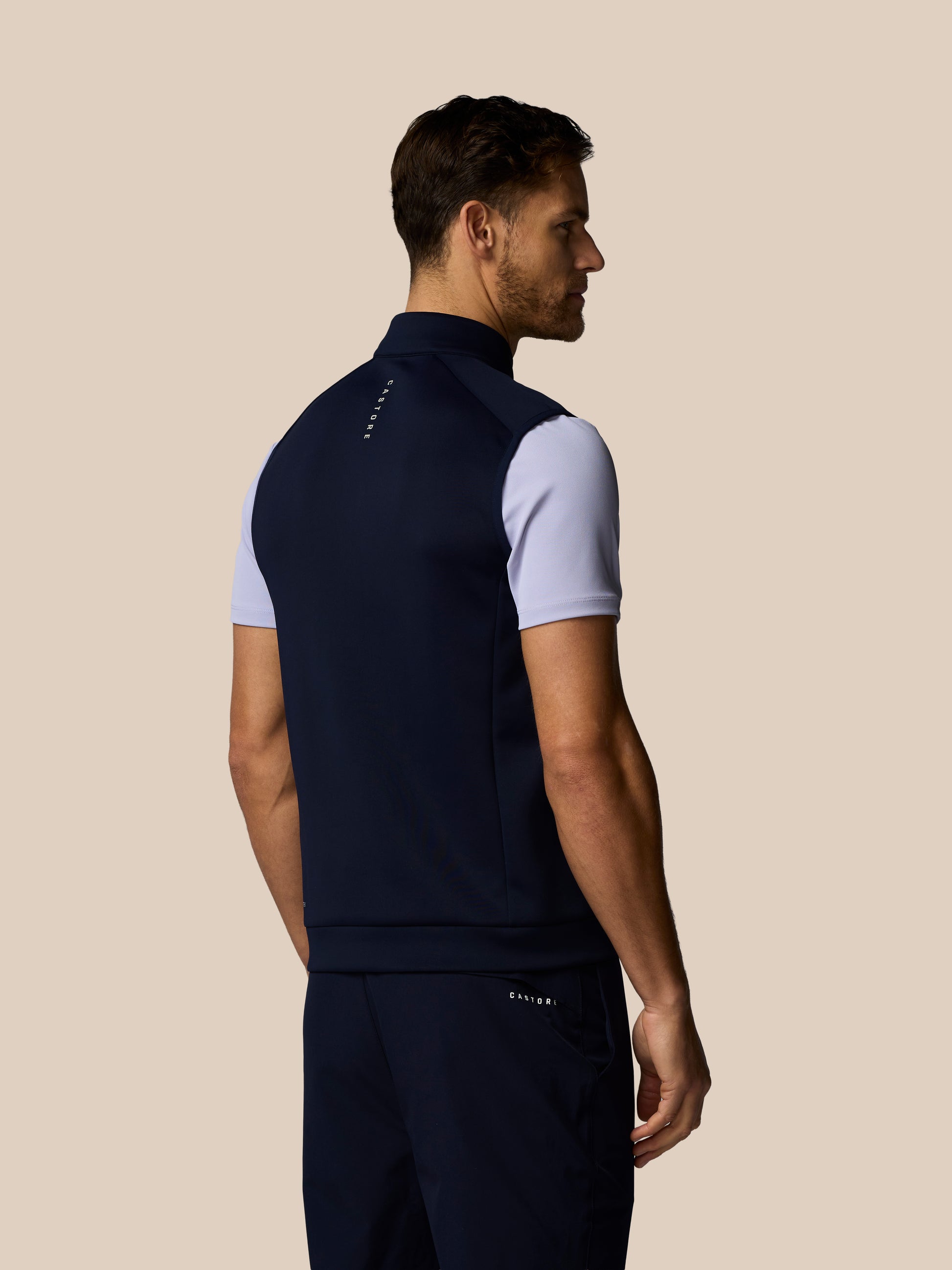 Rear view of a man wearing a navy Castore Golf Flex Half Zip Gilet with white sleeves and a wordmark on the upper back