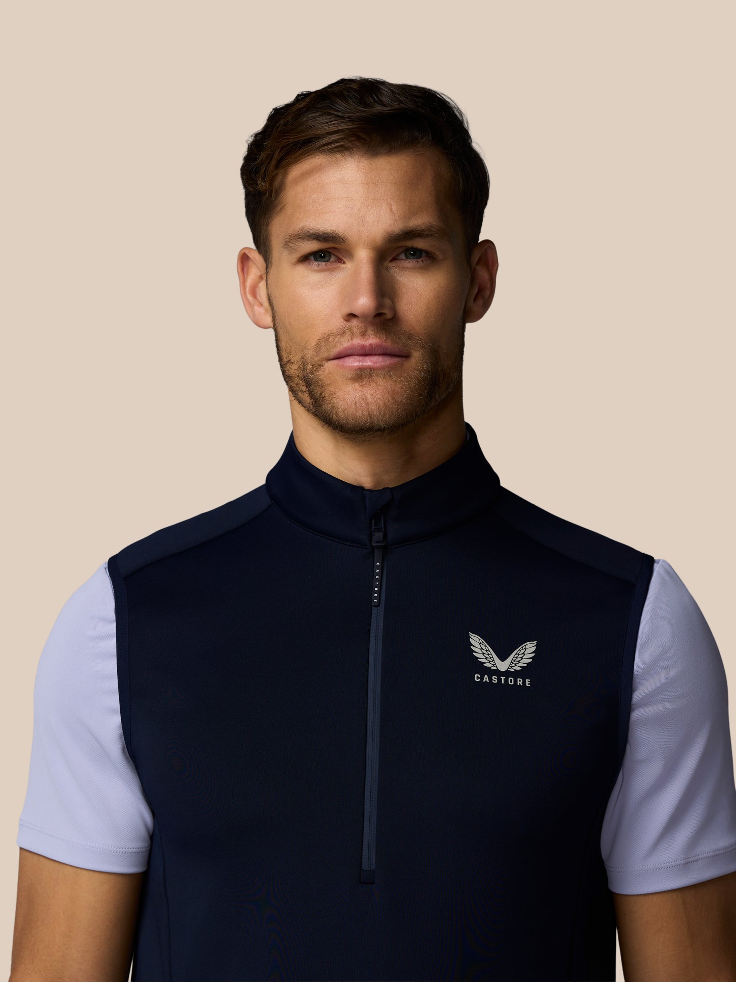Male model wearing navy golf Flex Half Zip Gilet with light blue sleeves, front zipper and Castore logo on chest.