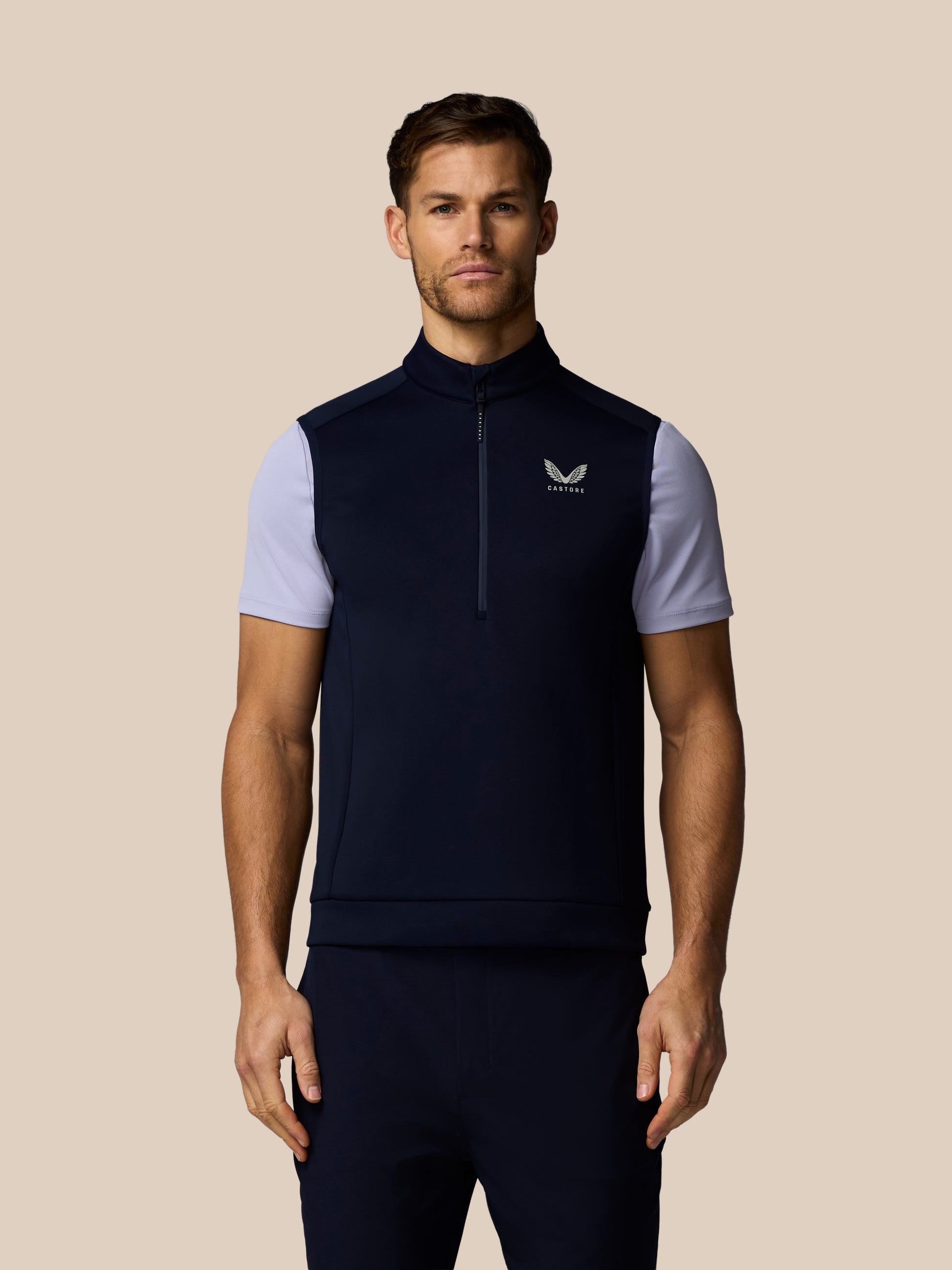 Front view of a man in navy Castore Golf Flex Half Zip Gilet with white sleeves and Castore logo on the chest