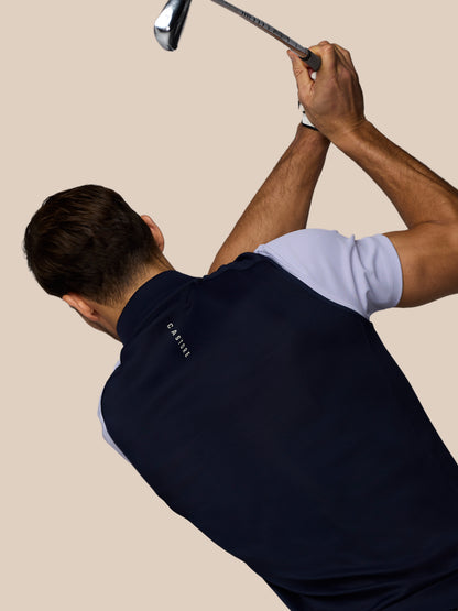 Male golfer wearing a navy Castore golf vest with arms raised in a backswing while gripping a club