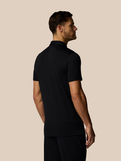 Back view of male model wearing black Castore golf polo with upper back branding against beige backdrop