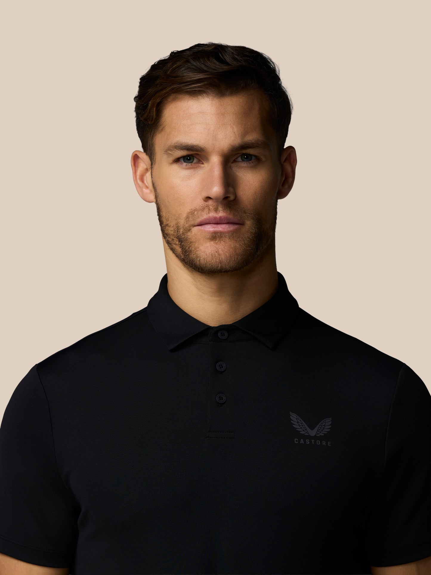 Portrait of a man wearing a black Castore golf polo against a beige background