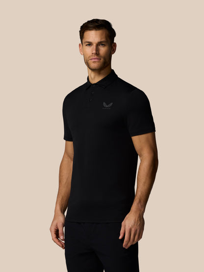 Man wearing black Castore golf polo with left chest logo and back wordmark, standing against a beige background