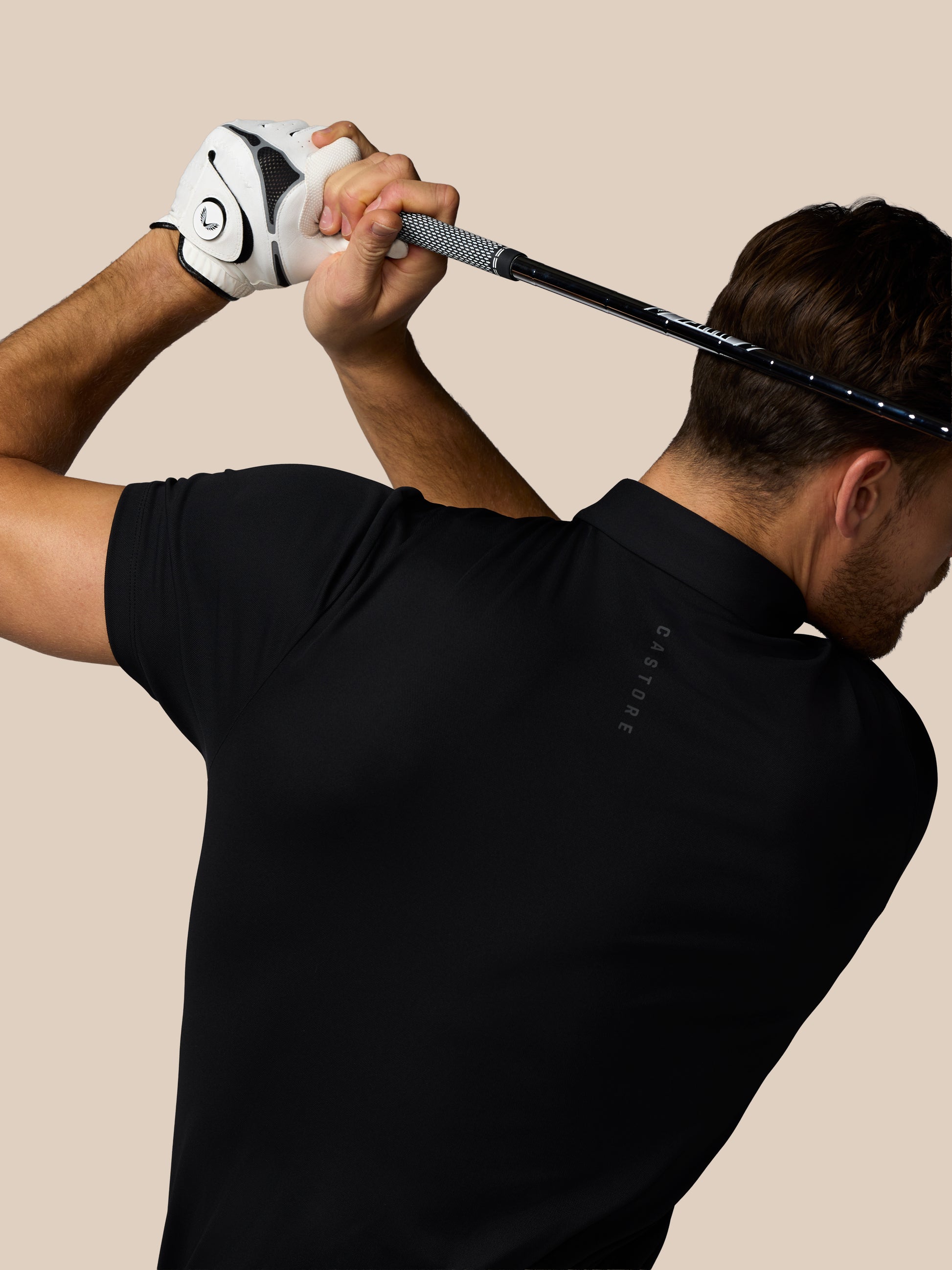 Model in black Castore golf polo showing left chest logo and front button placket