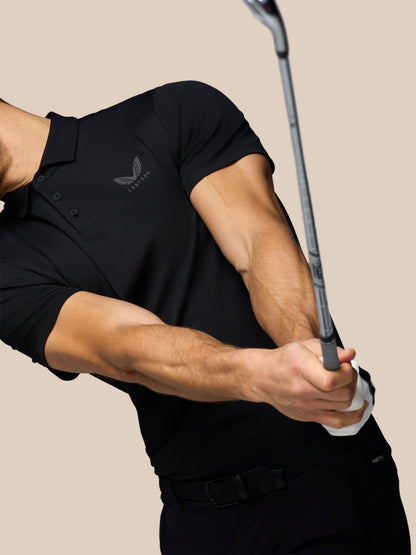 Athlete in black Castore polo mid swing, gripping a golf club with logo visible on chest
