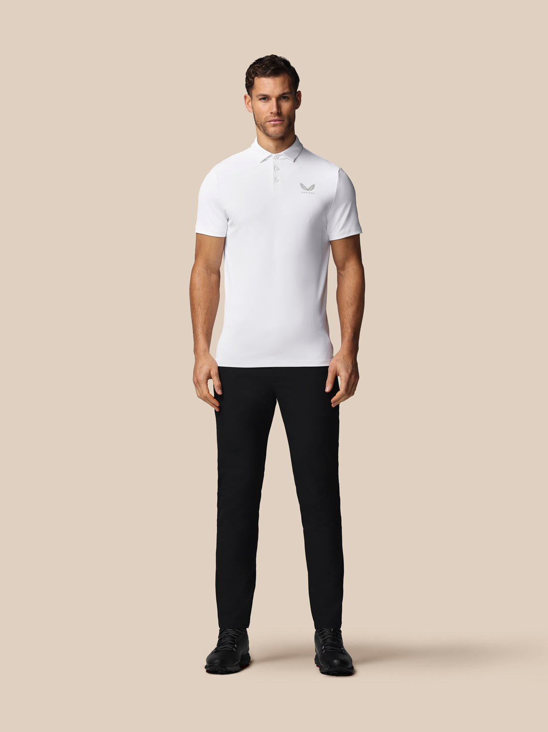 Man wearing a white polo shirt and black pants on a beige background