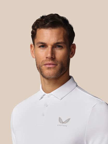 Man wearing a white polo shirt with a logo on a beige background