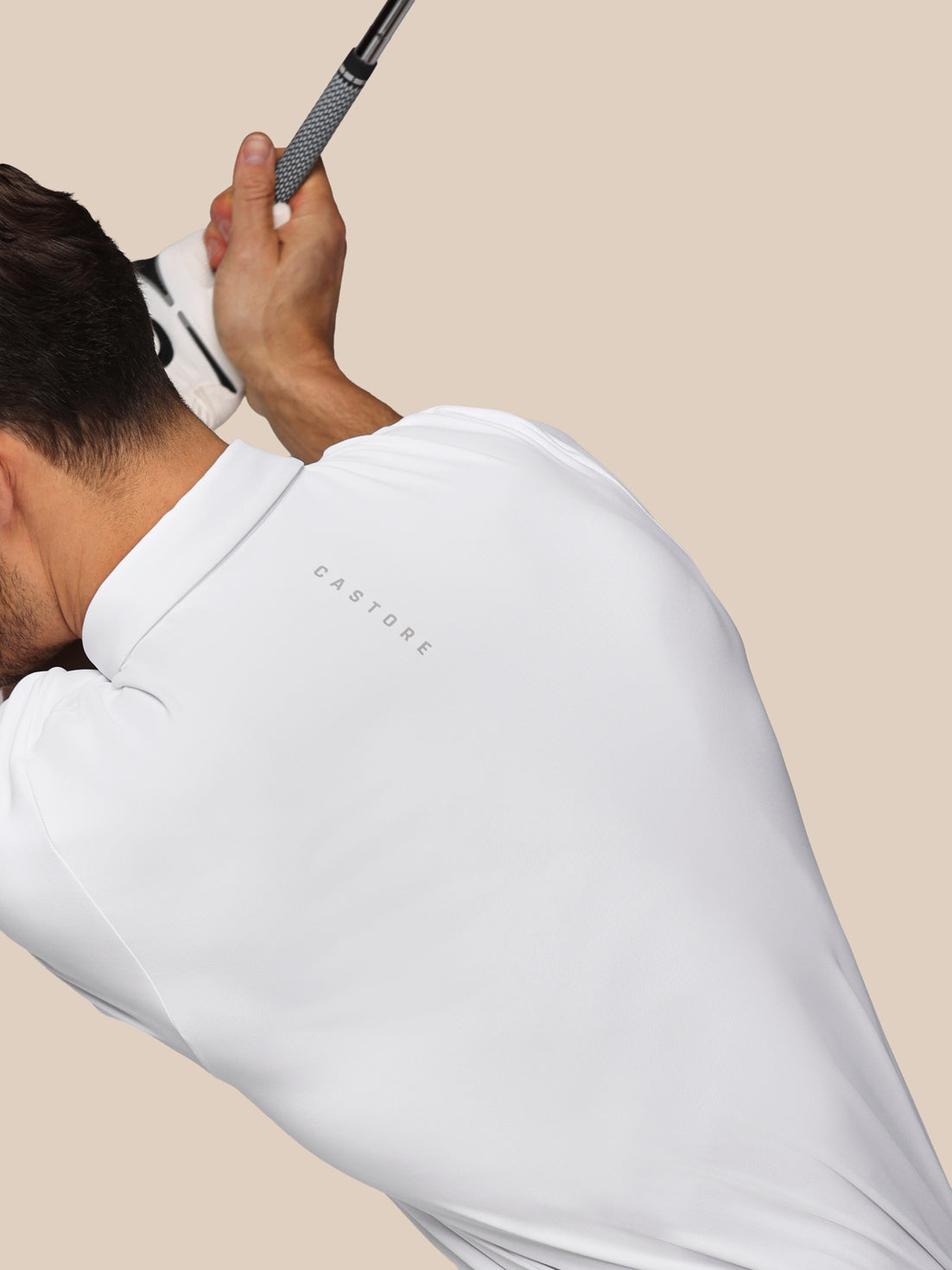 Person wearing a white polo shirt with 'Castore' branding, holding a golf club.