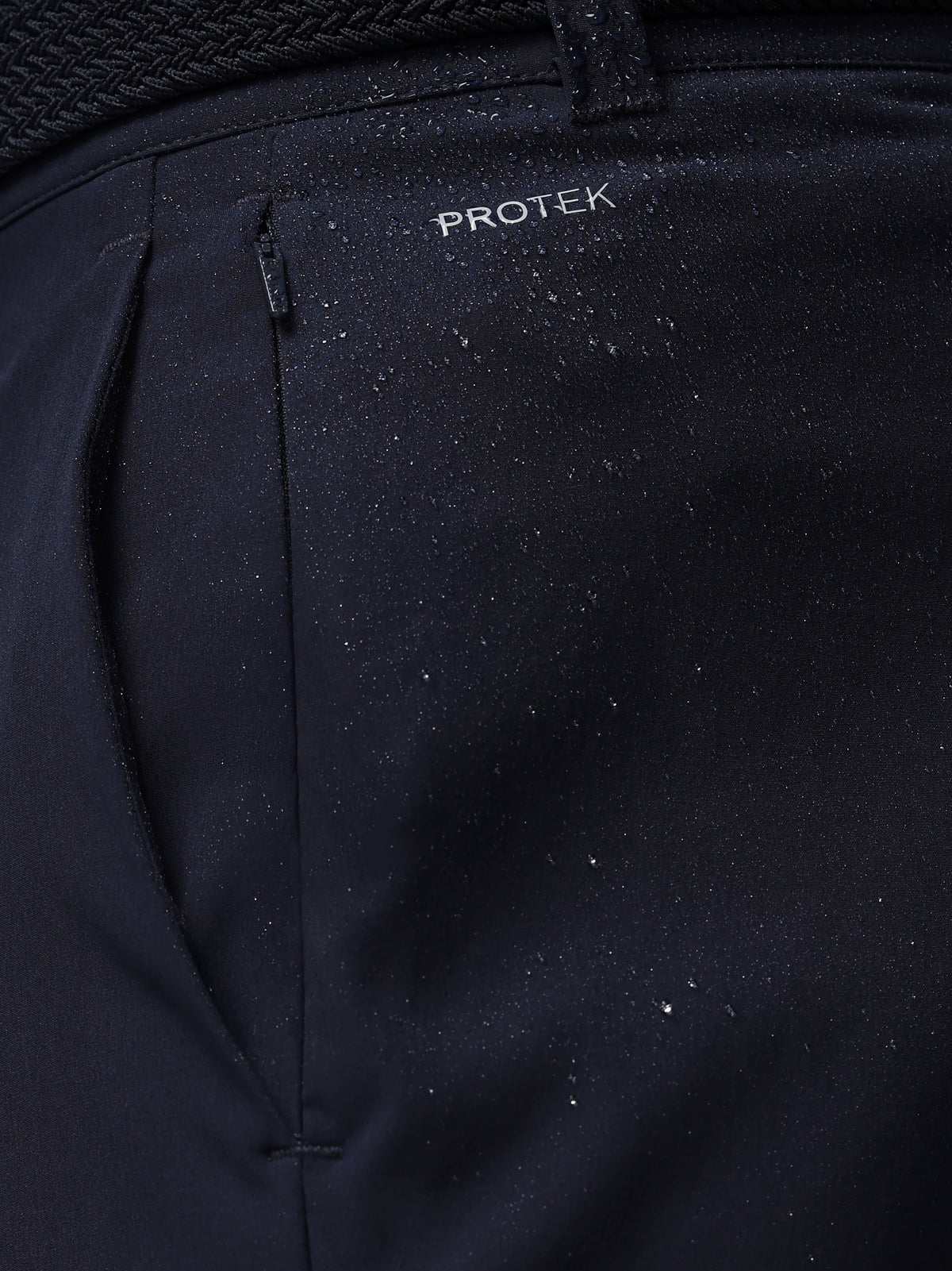Close-up of navy pants with 'PROTEK' branding on a dark background