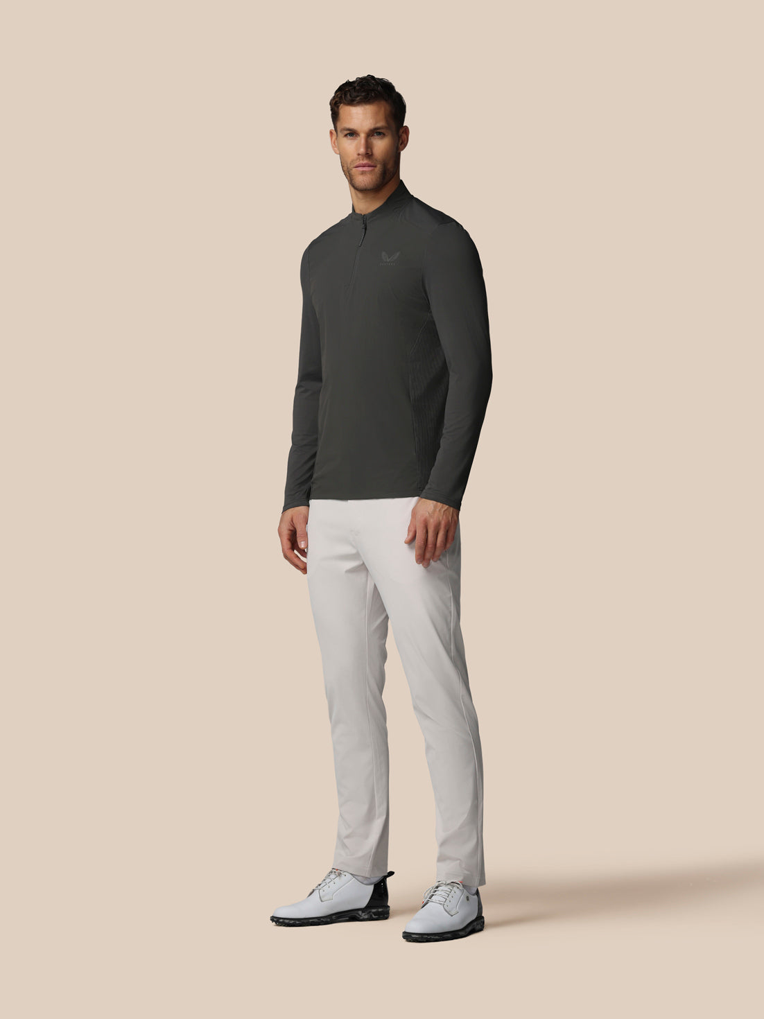 Male model wearing gunmetal LVS quarter zip golf top with mock neck and left chest logo, paired with white pants