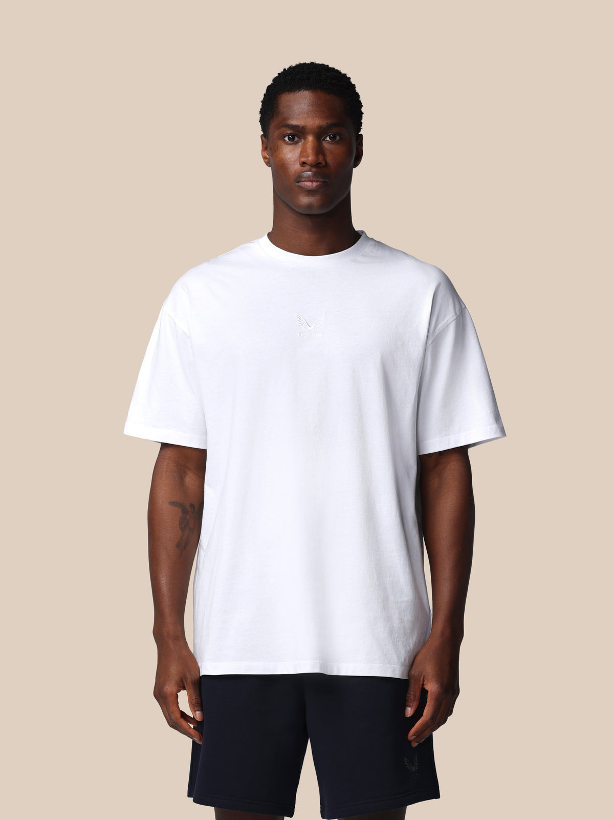 Man wearing a plain white t-shirt and black shorts on a beige background
