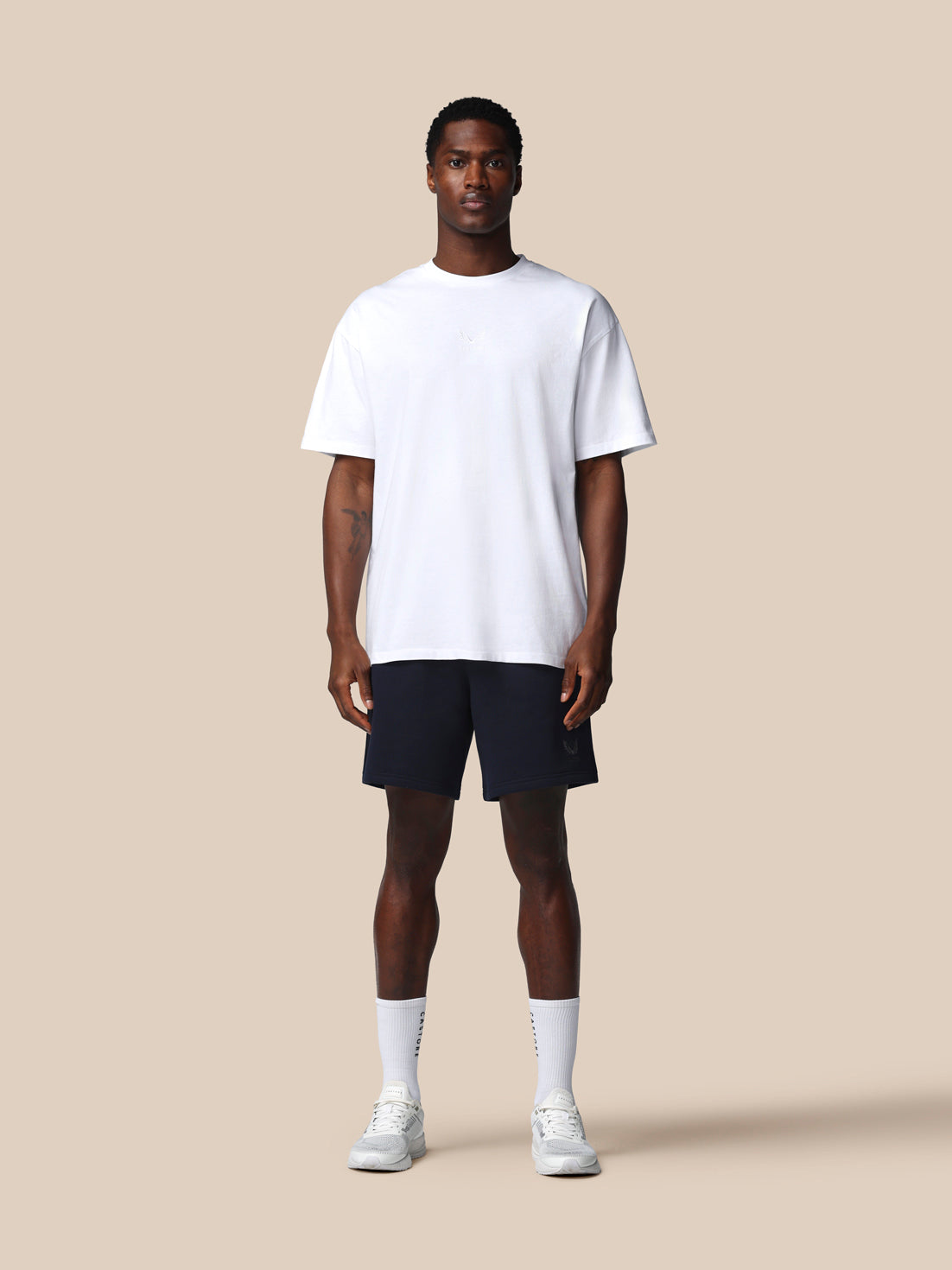 Man wearing a white t-shirt, black shorts, and white sneakers on a beige background