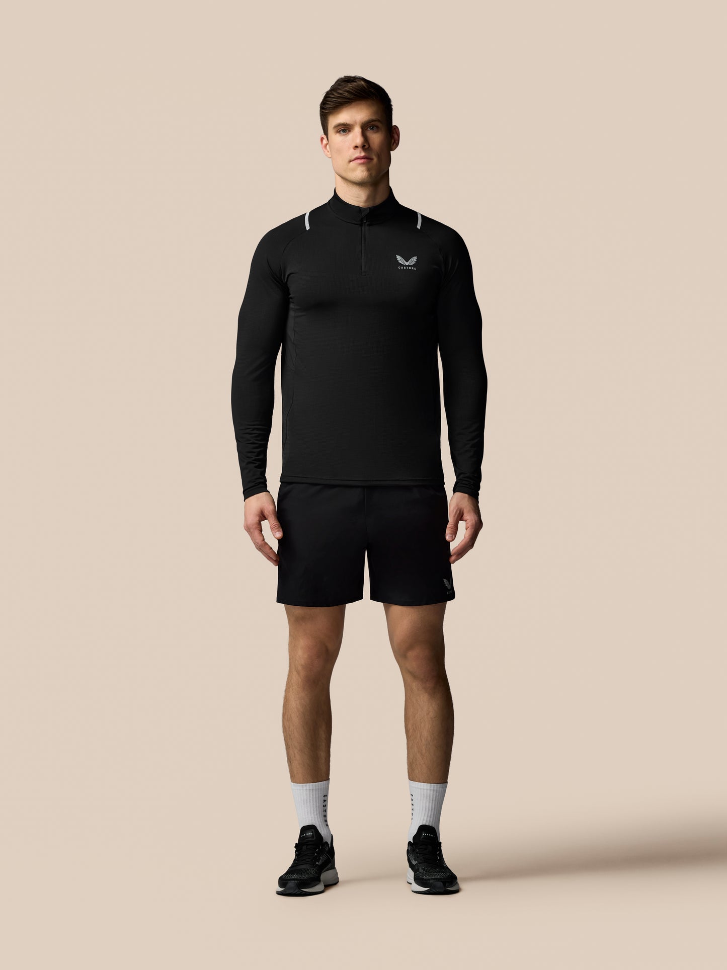 Male model in black Apex Training 1/4 zip top with long sleeves, high collar, reflective shoulder accents and Castore logo on chest